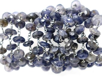 May include: A strand of dark blue faceted gemstone beads strung on a silver chain. The beads are oval shaped and have a slightly irregular shape.