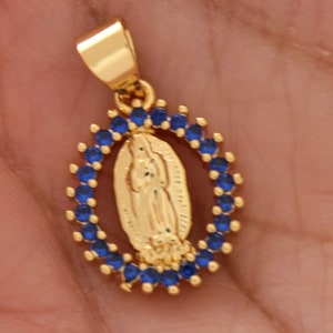 May include: Gold pendant with a blue crystal halo around a depiction of the Virgin Mary.