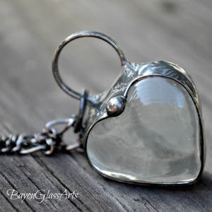 May include: A silver heart-shaped pendant necklace with a clear glass insert. The pendant is attached to a silver chain.