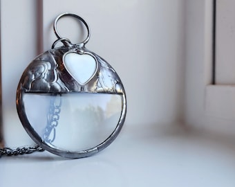May include: A silver-toned pendant with a heart-shaped pearl inlay and a magnifying glass lens. The pendant is attached to a silver chain.