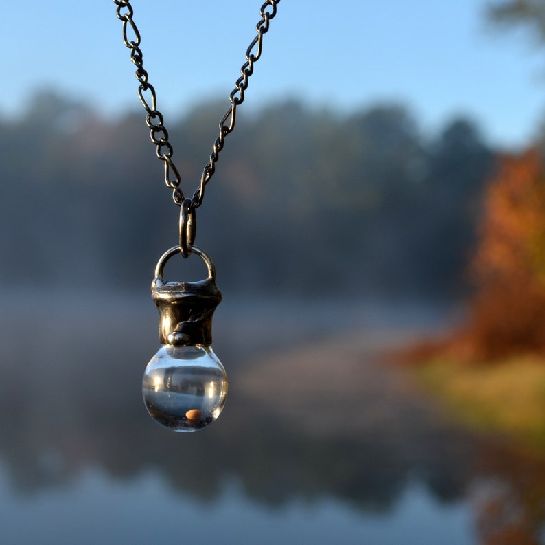 Mustard Seed Pendant Unisex Necklace Handmade by Louisiana Artisans at Bayou Glass Arts in USA. Glass bottle with seed enclosed by shiny black/aged silver metal hangs on fully adjustable gunmetal Figaro chain.