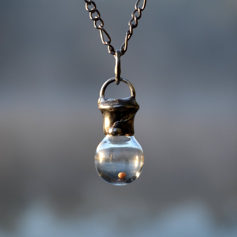 Mustard Seed Pendant Unisex Necklace Handmade by Louisiana Artisans at Bayou Glass Arts in USA. Glass bottle with seed enclosed by shiny black/aged silver metal hangs on fully adjustable gunmetal Figaro chain.