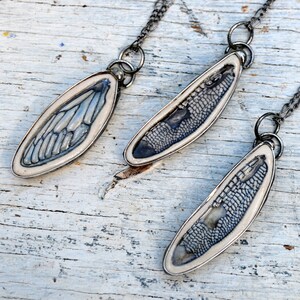 Three Handmade Insect Wing Pendants. Fire impressed on ceramic and encased in metal. First one is cicada, second is dragonfly in black, and third is dragonfly in blue.