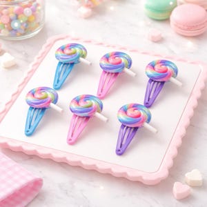 May include: Six colourful hair clips with lollipop designs. Each clip features a swirl of rainbow colours atop a pastel-coloured clip. The clips are arranged on a white surface with a pink scalloped border, suggesting a playful, whimsical theme.