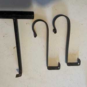 Puede incluir: Se muestran tres herramientas de metal negro sobre un fondo blanco. Las herramientas incluyen una barra en forma de T y dos ganchos curvos. Las herramientas parecen estar hechas de hierro forjado o un material similar, y probablemente se utilizan para una tarea específica.