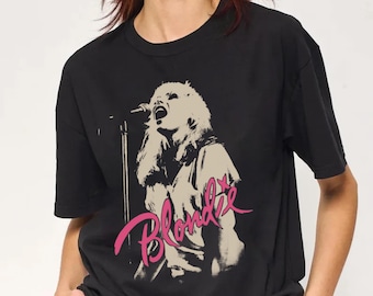 May include: A black short-sleeved t-shirt featuring a beige graphic print of a singer performing at a microphone stand. The word Blondie is printed in a stylized pink script font across the lower portion of the graphic design on the front.