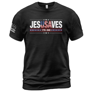 May include: A black short-sleeved t-shirt featuring the white text JESUSAVES with the USA letters stylized as an American flag. Below the text is 1776-2026 with a row of stars and stripes. A small graphic on the sleeve displays 1776 and We The People.