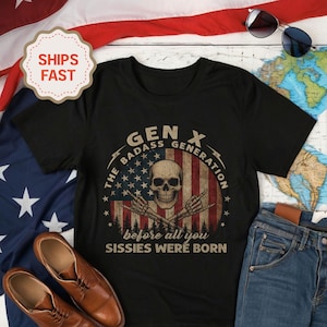 Peut inclure: T-shirt noir avec un motif graphique repr&eacute;sentant un cr&acirc;ne, le drapeau am&eacute;ricain et le texte "GEN X The Badass Generation" et "before all you sissies were born." Le t-shirt est pr&eacute;sent&eacute; avec des chaussures en cuir marron et un jean bleu.