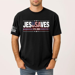 May include: A black short-sleeved t-shirt featuring the white text JESUSAVES across the chest, with the letters USA filled with a red, white, and blue American flag pattern. Below the text is 1776-2026 with stars and stripes, and a small 1776 logo on the sleeve.