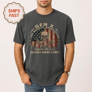 Peut inclure: T-shirt gris fonc&eacute; avec un motif vieilli repr&eacute;sentant un cr&acirc;ne, des os crois&eacute;s et un drapeau am&eacute;ricain. Le texte indique "GEN X The Badass Generation before all you Sissies Were Born."