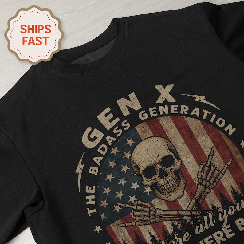 Peut inclure: Sweat-shirt noir &agrave; col rond avec un motif graphique repr&eacute;sentant un cr&acirc;ne, des mains de squelette et un drapeau am&eacute;ricain. Le texte indique "GEN X THE BADASS GENERATION".