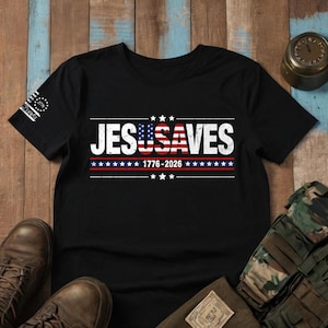 May include: A black short-sleeve t-shirt featuring the white text JESUSAVES with the USA portion stylized as an American flag. Below the text is 1776-2026 flanked by stars and horizontal lines. A small 1776 logo is printed on the left sleeve.