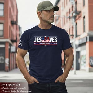 May include: A navy blue short-sleeved t-shirt featuring the white text JESUSA VES with the letters USA stylized as an American flag. Below the text is the date 1776-2026 with a row of stars. A small flag graphic is printed on the right sleeve.