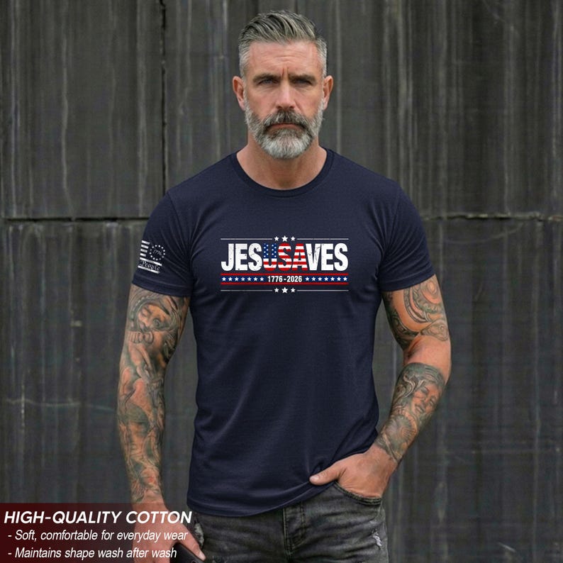 May include: A navy blue short-sleeved t-shirt featuring the white text JESUSA VES with the letters USA stylized as an American flag. Below the text is 1776-2026 in white, flanked by red and white stripes and blue stars. A small flag emblem is on the sleeve.