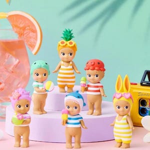 May include: Six small collectible figurines standing on a tiered display. The figures wear various headgear including a pineapple, shark, octopus, and bunny ears, paired with striped outfits. They hold miniature items like ice cream and a beach ball.
