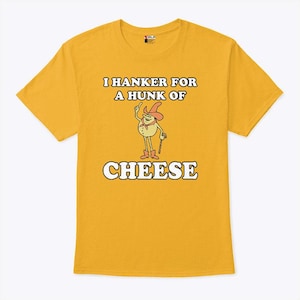 以下が含まれることがあります： マスタードイエローのTシャツ。テキストは「I HANKER FOR A HUNK OF CHEESE」。帽子とブーツを履き、杖を持っているキャラクターの漫画イラストが特徴です。テキストとイラストは白と茶色です。