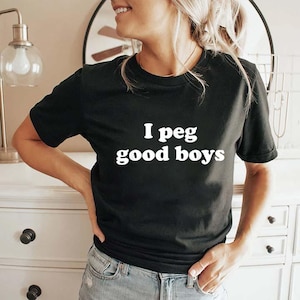 Puede incluir: Camiseta negra de cuello redondo con el texto blanco "I peg good boys". La camiseta está hecha de un material suave y es adecuada para ropa casual. El texto está centrado en la parte delantera de la camiseta.