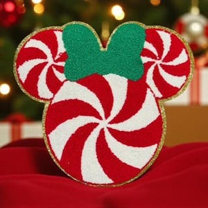 May include: A festive Christmas ornament in the shape of Mickey Mouse's head, designed with red and white candy cane stripes. The ornament features a green bow and is outlined with gold glitter. Perfect for holiday decor.