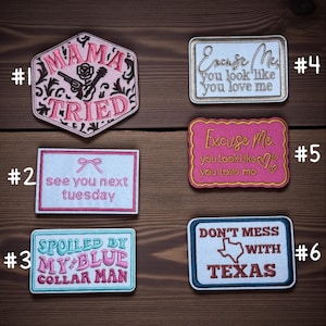 May include: A selection of embroidered patches with different designs and text. The patches feature phrases such as "Mama Tried," "See You Next Tuesday," "Spoiled by My Blue Collar Man," "Excuse Me, You Look Like You Love Me," and "Don't Mess with Texas."