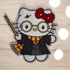 May include: A white, glitter-edged patch featuring a cartoon cat character with a red bow, round glasses, and a lightning bolt. The cat wears a black robe and a red and yellow scarf, holding a yellow wand. The design is a mashup of the character and a wizard theme.