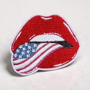 Op de afbeelding: Geborduurde patch met rode lippen en een witte rand. De tong toont het ontwerp van de Amerikaanse vlag met blauwe sterren en rode en witte strepen. De patch is geschikt om op stof te strijken of te naaien.
