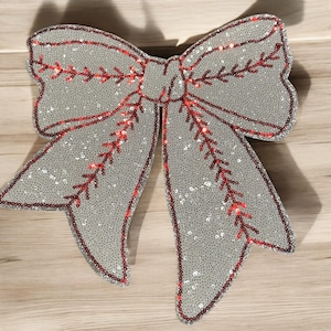 Könnte beinhalten: Eine große, dekorative Schleife mit Paillettenmuster. Die Schleife ist hauptsächlich silberfarben mit roten Akzenten, die die Ränder und die Mitte umranden. Die Schleife besteht aus vielen kleinen Pailletten und wird wahrscheinlich für Feiertags- oder Eventdekorationen verwendet.