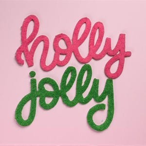 Puede incluir: Fondo rosa con las palabras "holly jolly" en fuente cursiva. La palabra "holly" es de color rosa texturizado, y "jolly" es de color verde texturizado. Las letras están ligeramente en relieve, dando un efecto 3D.