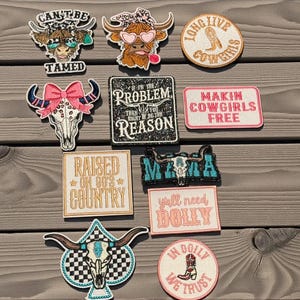 Puede incluir: Una colección de parches bordados con temática country y western. Los diseños incluyen una calavera de cuernos largos con un lazo rosa, una bota y frases como "Makin Cowgirls Free" y "Raised on 80's Country".