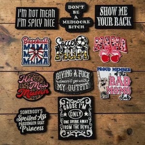 Op de afbeelding: Een verzameling geborduurde patches met verschillende zinnen en ontwerpen. De patches bevatten teksten als "I'm not mean, I'm spicy nice", "Show me your rack" en "Giving a fuck doesn't go with my outfit". Andere patches bevatten een voetbalmoeder-ontwerp en een "Bad Moms Club"-patch.