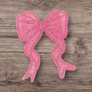 Könnte beinhalten: Eine rosa Glitzer-Schleife mit fließenden Bändern. Die Schleife hat ein strukturiertes, funkelndes Aussehen. Die Schleife ist auf einer Holzoberfläche zentriert.