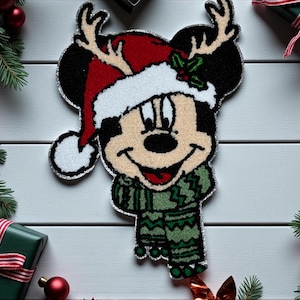 Puede incluir: Un diseño festivo de Mickey Mouse, con un gorro de Papá Noel rojo y blanco con cuernos, una bufanda verde y un suéter a juego. La imagen está rodeada de decoraciones navideñas, incluyendo adornos y cajas de regalo.
