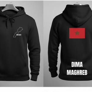 May include: Black hoodie with a front pocket and a hood. The front features a white outline of Morocco with "CAN 2025" below it. The back displays the Moroccan flag and the words "DIMA MAGHREB" in white.