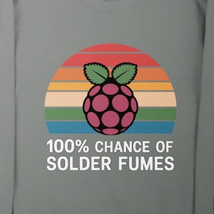 May include: Gray sweatshirt with a graphic of a raspberry and a sunset design. The text "100% CHANCE OF SOLDER FUMES" is printed below the graphic. The sweatshirt is on a wooden surface.