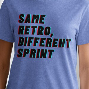 May include: A blue t-shirt with the text "SAME RETRO, DIFFERENT SPRINT" in a 3D effect. The text is in black, red, and blue. The shirt is short-sleeved and made of a soft material.