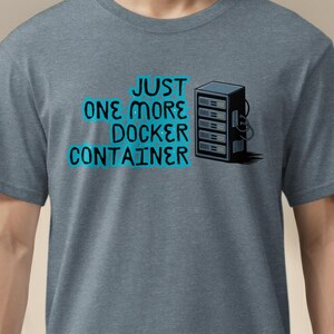 May include: A heather gray t-shirt with the text "JUST ONE MORE DOCKER CONTAINER" in teal and a black and white server graphic. The shirt is short-sleeved and has a crew neck.