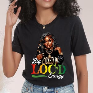 May include: Black t-shirt featuring a graphic of a woman with long locs, gold jewelry, and the text "Big Locked In Loc'd Energy" in red, yellow, and green. The shirt is made of a soft material.