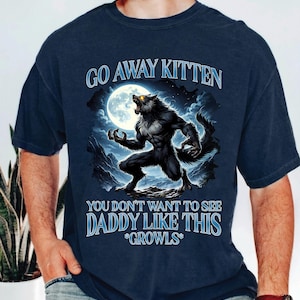 May include: Navy blue t-shirt featuring a werewolf illustration under a full moon. The text reads "GO AWAY KITTEN, YOU DON'T WANT TO SEE DADDY LIKE THIS *GROWS*". The design is a fantasy theme.