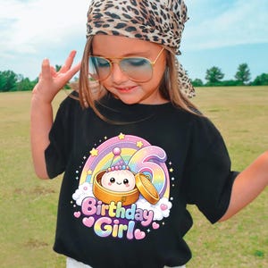 Pu&ograve; includere: Una t-shirt nera con la grafica di un grazioso raviolo al vapore in un cestello di bamb&ugrave;, un arcobaleno e il numero sei. Il testo "Birthday Girl" &egrave; stampato in lettere colorate a bolla sotto l'illustrazione, circondato da piccole stelle e cuori.