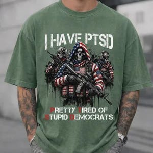May include: Green t-shirt with the text "I HAVE PTSD" above a graphic of three soldiers with skull faces, one draped in an American flag. The text "PRETTY TIRED OF STUPID DEMOCRATS" is below the graphic.