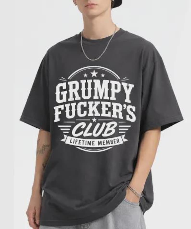 May include: Dark grey t-shirt with the text "GRUMPY FUCKER'S CLUB LIFETIME MEMBER" in white. The graphic is centered on the front of the shirt. The shirt has short sleeves and a crew neck.