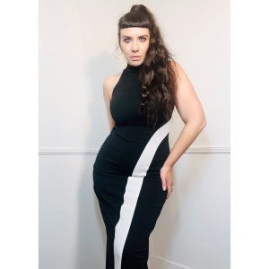 May include: A woman wearing a black and white dress with a high neckline and a diagonal white stripe. The dress is fitted and has a long skirt.