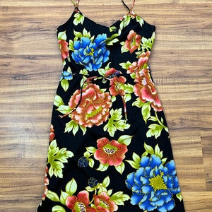 May include: A black midi dress with a floral print featuring red, pink, blue, and green flowers. The dress has thin straps and a tie at the waist.