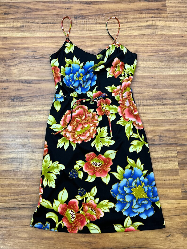 May include: A black midi dress with a floral print featuring red, pink, blue, and green flowers. The dress has thin straps and a tie at the waist.