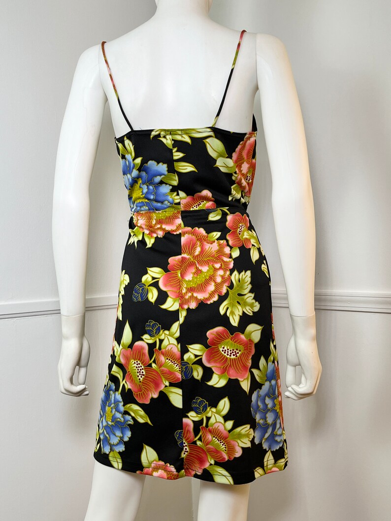 May include: A black sleeveless dress with a floral print featuring large red, pink, blue, and green flowers. The dress has a scoop neck and a fitted silhouette.