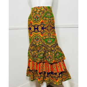 May include: A vibrant, patterned skirt with a tiered, ruffled hem. The skirt features a colorful paisley design in shades of blue, green, orange, and yellow. The skirt is displayed on a mannequin.