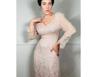 Puede incluir: Un vestido largo de lentejuelas de color rosa pálido. El vestido tiene un escote en V y una silueta ajustada. Las lentejuelas son iridiscentes y crean un efecto brillante.