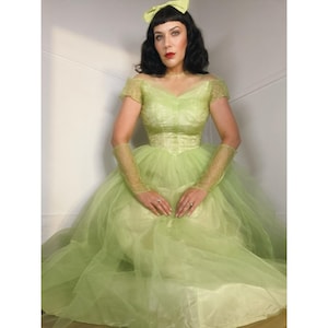 May include: A light lime green dress featuring a fitted bodice with short sleeves, a full tulle skirt, and matching lace gloves. The garment includes a pale green hair bow accessory. The dress has a sweetheart neckline and a layered tulle overlay.