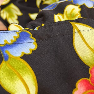 May include: Black fabric with a floral pattern in shades of blue, yellow, and pink. The fabric has a subtle sheen and a textured surface.