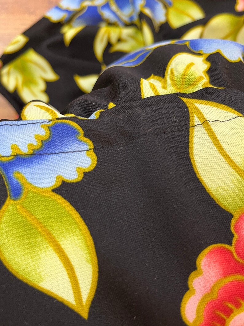 May include: Black fabric with a floral pattern in shades of blue, yellow, and pink. The fabric has a subtle sheen and a textured surface.