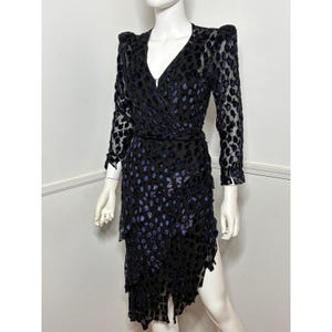 Könnte beinhalten: Schwarzes Wickelkleid mit langen Ärmeln und V-Ausschnitt. Das Kleid hat ein Muster aus blauen Punkten und einen asymmetrischen, geschichteten Saum. Das Kleid wird auf einer Schaufensterpuppe präsentiert.